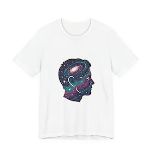 May include: White t-shirt featuring a graphic of a person's profile with a galaxy design inside the silhouette. The galaxy design includes swirls of purple, blue, and teal with white stars. The shirt is made of a soft material.
