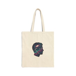 Peut inclure: Sac fourre-tout crème avec le profil d'une tête humaine remplie d'un motif de galaxie violet, bleu et vert. Le sac a de longues anses et un design simple et minimaliste.