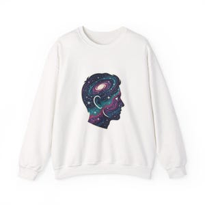 Peut inclure: Un sweat-shirt blanc avec un motif de profil de personne, la tête remplie d'un motif de galaxie. La galaxie présente des tourbillons de bleu, de violet et de rose, avec des étoiles blanches. Le sweat-shirt a un col rond et des manches longues.