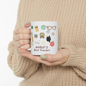 Peut inclure: Mug en céramique blanche avec le texte "WORLD'S Best Teacher" et des illustrations colorées d'objets scolaires. La tasse présente des images d'un crayon, de livres, d'un globe, de lunettes, d'un bus scolaire et d'une pomme.