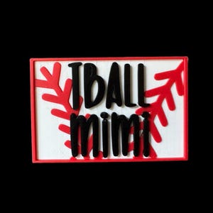 May include: A rectangular wooden sign with the words "I BALL MIMI" in black, set against a white background. The sign is framed in red, with red snowflake-like accents on the sides. The sign is likely a decorative item.