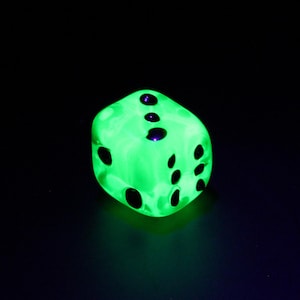 Peut inclure: Un dé vert fluorescent avec des points noirs sur fond noir. Le dé est éclairé, les points sont clairement visibles. Accessoire de jeu.