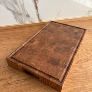 Puede incluir: Tabla de cortar rectangular de madera marr&oacute;n oscuro con veta de extremo. Tiene un canal para jugos y un asa recortada. El patr&oacute;n de la veta de la madera es visible en toda la tabla. Mide aproximadamente 30 cm x 45 cm.