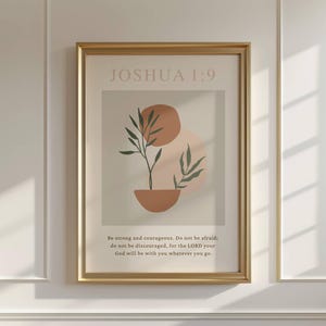 May include: A beige printable wall art print with a gold frame. The print features a minimalist design with a green plant, brown and peach circles, and the text "JOSHUA 1:9" in black. The text below the design reads "Be strong and courageous. Do not be afraid; do not be discouraged, for the LORD your God will be with you wherever you go."