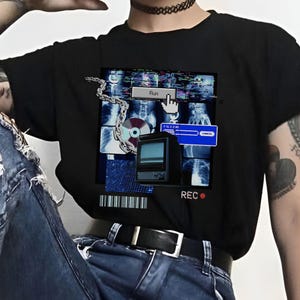 May include: A black t-shirt featuring a graphic print of a computer screen with a blue and white interface. The graphic includes the text "Run" and "REC". The person wearing the shirt is also wearing blue jeans with rips and black fishnet tights.