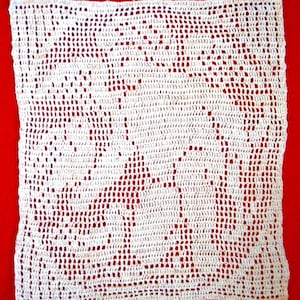 May include: A white, rectangular, crocheted doily with an openwork design. The doily features a repeating pattern of stylized trees and geometric shapes. The background is a solid red color.