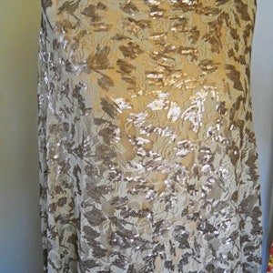 Puede incluir: Una tela beige transparente con un patrón floral y lentejuelas doradas. La tela está drapeada sobre un maniquí.