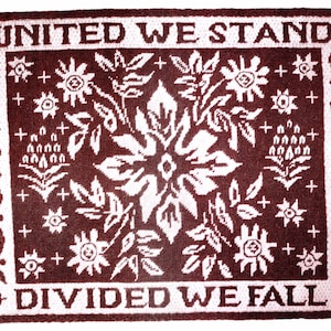Puede incluir: Una alfombra tejida marrón y blanca con un diseño floral y el texto "United We Stand" y "Divided We Fall".