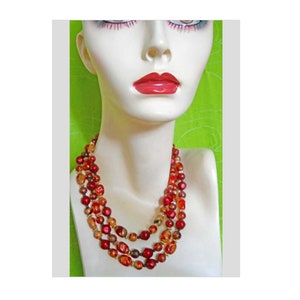 May include: A three-strand necklace made of red, orange, and gold beads. The beads are round and have a slightly iridescent finish.
