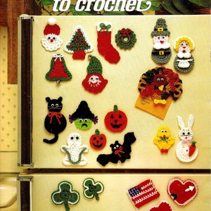 May include: A collection of 22 crochet fridge magnets with various holiday themes, including Christmas, Halloween, Thanksgiving, and Valentine's Day. The magnets are displayed on a white refrigerator.