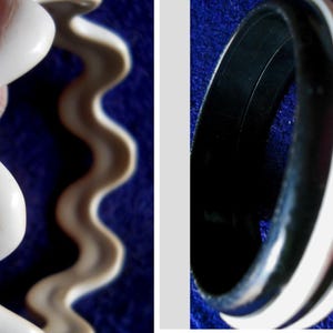 May include: Two bracelets are shown. One is a wavy, off-white color. The other is a black and white striped bangle. The background is a dark blue color.