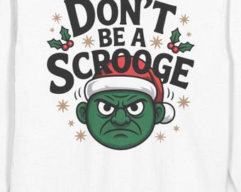 May include: White long-sleeved top with the slogan "Don't Be a Scrooge." The graphic shows a green face in a Santa hat, with holly and stars. A festive Christmas-themed shirt.
