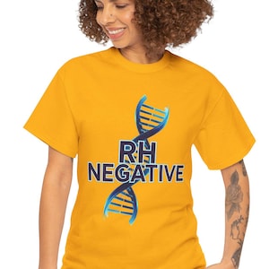 May include: Mustard yellow t-shirt with a blue and white DNA strand design and the text "RH NEGATIVE". The shirt has short sleeves. The model is wearing blue jeans. The shirt is made of a soft material.