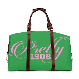 May include: Green travel duffel bag with brown leather handles and straps. The bag has the words "Pretty 1908" printed on the front in pink.