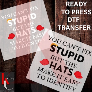 May include: DTF transfer with the text "YOU CAN'T FIX STUPID BUT THE HATS MAKE IT EASY TO IDENTIFY". The design includes red baseball caps and a yellow hair graphic. The words "READY TO PRESS DTF TRANSFER" are also visible.
