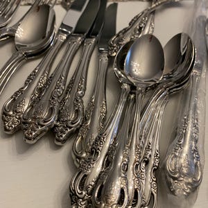 May include: A set of silver-plated silverware with ornate handles. The silverware includes knives, forks, and spoons.