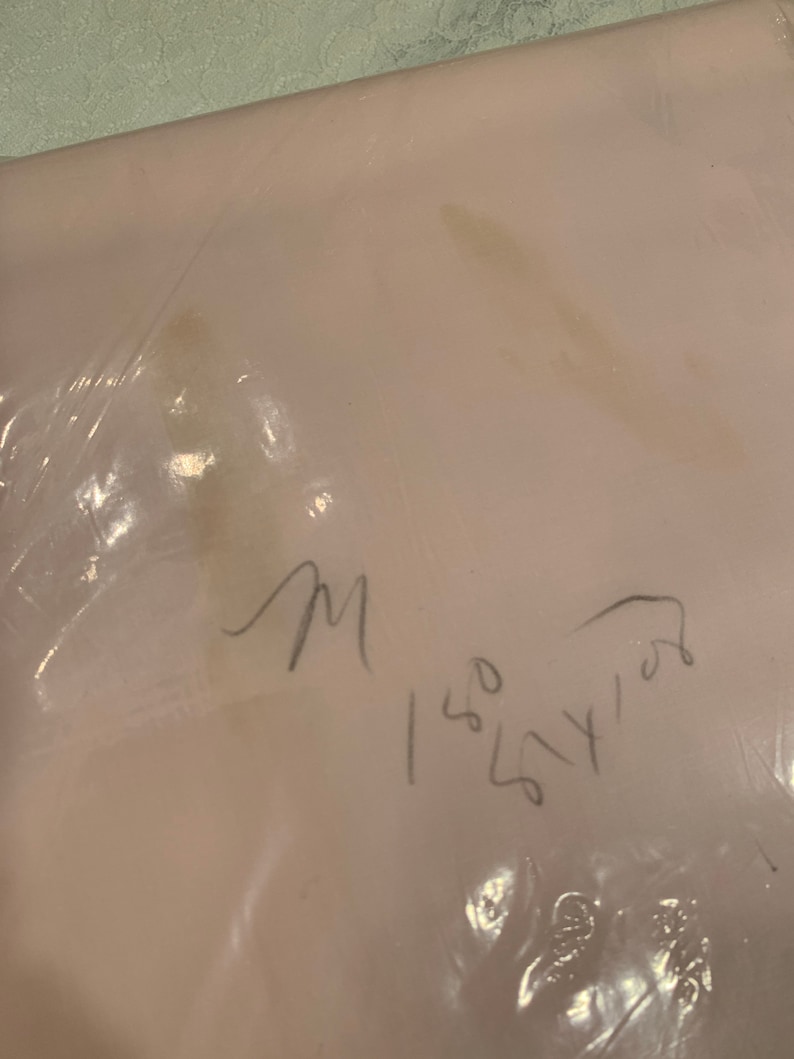 May include: A close-up of a light pink fabric with a handwritten note that says "M 150 54 102".