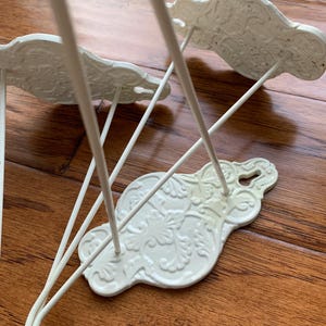 May include: White metal towel rack with three decorative hooks. Each hook features a floral design.