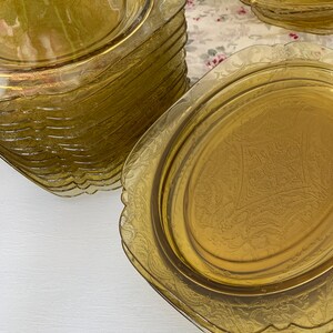 May include: A stack of amber glass plates with a scalloped edge and an intricate floral design. The plates are stacked on a white surface.