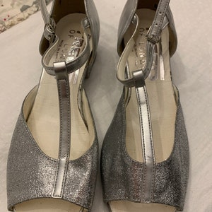 May include: A pair of silver glitter open-toe heeled sandals with ankle straps. The sandals have a T-strap design and the brand name "FRED OF LONDON" is printed on the insole.