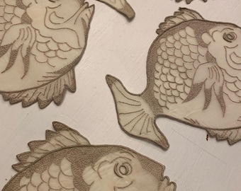 May include: Four beige fish-shaped decorative items with detailed embroidered outlines. The fish have scales, fins, and expressive eyes. The items are arranged on a white surface, creating a whimsical and aquatic theme.