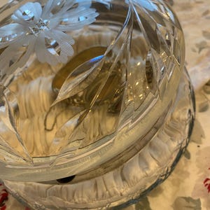 May include: A clear glass trinket box with an etched floral design and a silver hinged lid. The box is filled with a white fabric lining and a silver chain necklace.