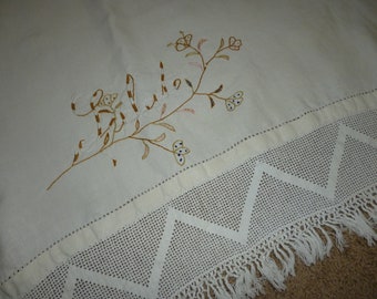 May include: White embroidered tablecloth with a floral design and the word "Hello" in brown thread. The tablecloth has a crocheted border with a fringe.