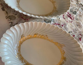 May include: Two white oval serving bowls with a gold rim and a gold floral design. The bowls have a fluted edge.