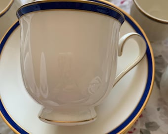 May include: A set of white teacups and saucers with a blue and gold trim. The cups have a classic shape and are perfect for a formal tea party.