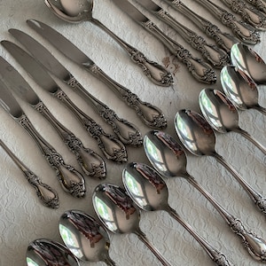 May include: A set of silverware with ornate handles. The set includes both knives and spoons, all made of polished stainless steel.
