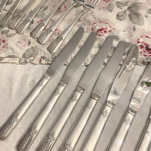 May include: A set of vintage silverware, including forks and knives, with ornate floral designs. The silverware is made of polished silver and has a classic, elegant style.