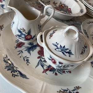 May include: A set of white porcelain dishes with a floral pattern in shades of blue, red, and yellow. The dishes include a large platter, a creamer, a sugar bowl with a lid, and a small bowl.