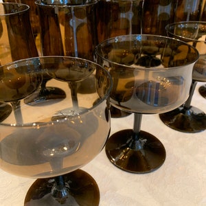May include: A set of brown glass wine glasses with a wide bowl and a tall stem. The glasses are arranged in a row on a white tablecloth.