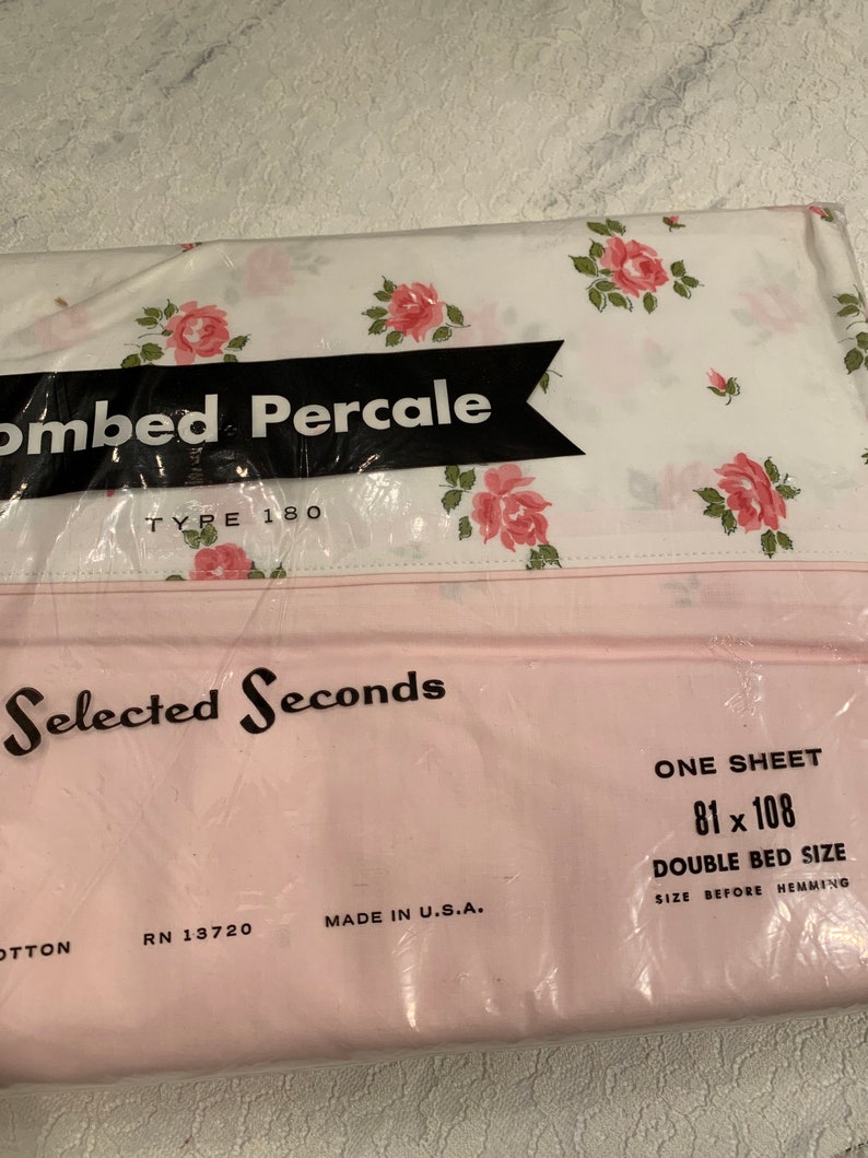 May include: A pink and white floral patterned sheet in a plastic bag. The bag has the text "Combed Percale Type 180" and "Selected Seconds". The sheet is labeled as "One Sheet 81 x 108 Double Bed Size Size Before Hemming".
