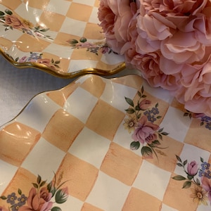 May include: Two ceramic serving dishes with a checkered pattern in white and light peach. The dishes have a scalloped edge and are decorated with floral designs in shades of pink, purple, and yellow.