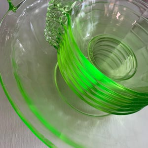May include: A set of two translucent lime green glass dishes. The larger bowl features a wide rim and a decorative handle with a textured, fan-like pattern. The smaller bowl is nested inside, displaying horizontal ribbed lines and a matching handle.