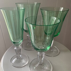 May include: Four green glass wine glasses with clear stems and bases. The glasses are arranged on a white surface.