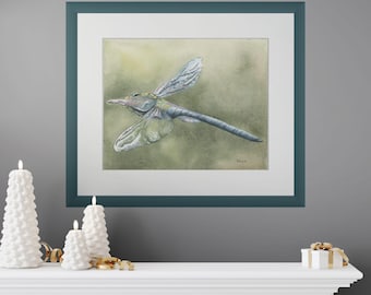 May include: A framed watercolor painting of a dragonfly. The dragonfly is depicted in shades of blue, green, and gray, with delicate wings. The artwork is set against a soft, muted green background, framed in a teal border.