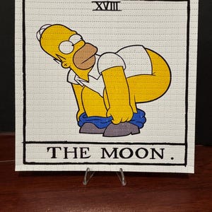 May include: A yellow cartoon character with blue pants is depicted on a white card with black text. The card is labeled "XVIII THE MOON."
