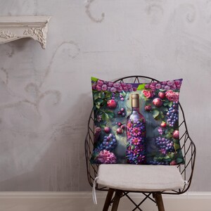 Op de afbeelding: Een decoratief kussen met een kleurrijk ontwerp met een wijnfles omringd door druiven, bloemen en bladeren. De fles is versierd met paarse en roze bloemen. De achtergrond is donkerblauwgrijs.