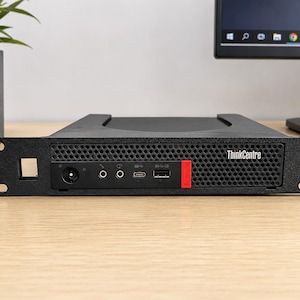 Può includere: Un computer ThinkCentre nero con un accento rosso, dotato di più porte e del logo ThinkCentre. Il computer è montato in un rack e si trova su una superficie di legno di colore chiaro.