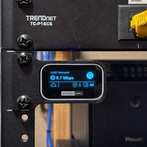 May include: A white ceramic mug with a black handle and the text "But First, Coffee" in a bold, black font. The mug is set against a blurred background, suggesting a cozy setting.