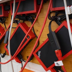 May include: A collection of red and black electronic devices with attached cables and cords. The devices are mounted on a wooden surface. Some devices have the "ThinkPad" logo and "Dell" branding.