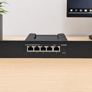 Puede incluir: Un conmutador de escritorio Gigabit de 5 puertos TP-Link modelo TL-SG1005S negro con placa frontal para montaje en rack. El panel frontal cuenta con cinco puertos Ethernet numerados del uno al cinco, un indicador Link/Act y un LED verde.