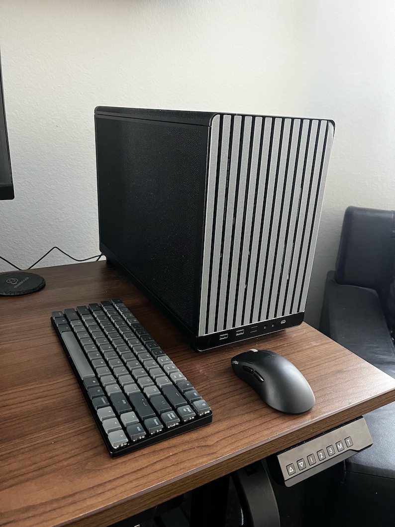 May include: A black and silver computer case with a vertical striped design sits on a wooden desk. A gray keyboard and mouse are positioned in front of the case. The desk has a control panel for height adjustment.