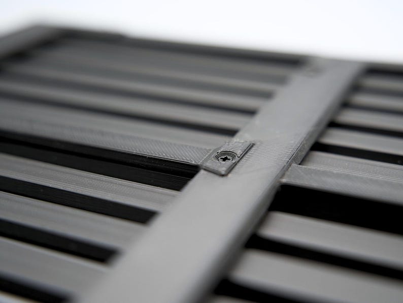 May include: Close-up of a gray, slatted object with a crossbar secured by a screw. The object has a series of parallel, dark gray slats. The crossbar is a lighter shade of gray.
