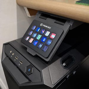 May include: A black Stream Deck control panel with multiple illuminated buttons, displaying various app icons. The panel is angled and positioned above a black computer case, with USB ports and a power button visible.