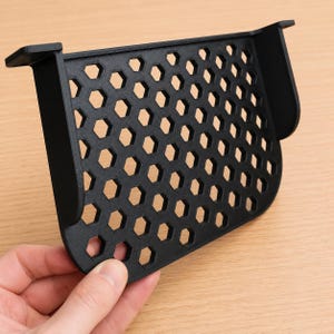 Peut inclure: Une étagère en plastique noir imprimée en 3D présentant un motif hexagonal en nid d'abeille sur toute sa surface plane, avec deux panneaux latéraux et des supports de fixation supérieurs s'étendant pour permettre une installation murale.