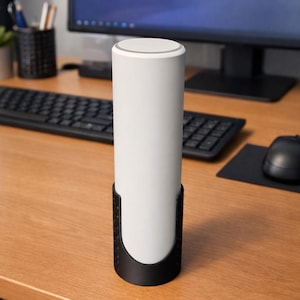 May include: A white cylindrical device in a black cradle sits on a wooden desk. The device has a rounded top and a black base. A computer monitor, keyboard, and mouse are in the background.