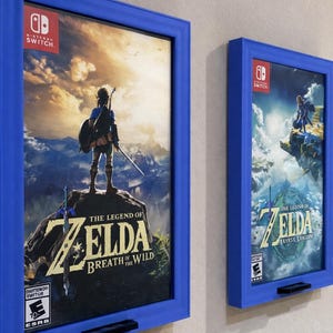 May include: Two framed Nintendo Switch game covers. The blue frames hold "The Legend of Zelda: Breath of the Wild" and "Tears of the Kingdom" artwork. The games' titles are visible, along with the Nintendo Switch logo and ESRB ratings.